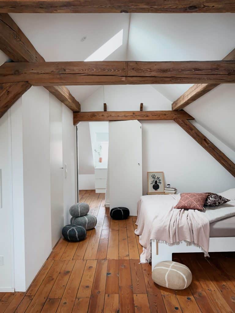 Schlafzimmer in ausgebautem Dachgeschoss mit Holzbalken und Poufs aus Filz