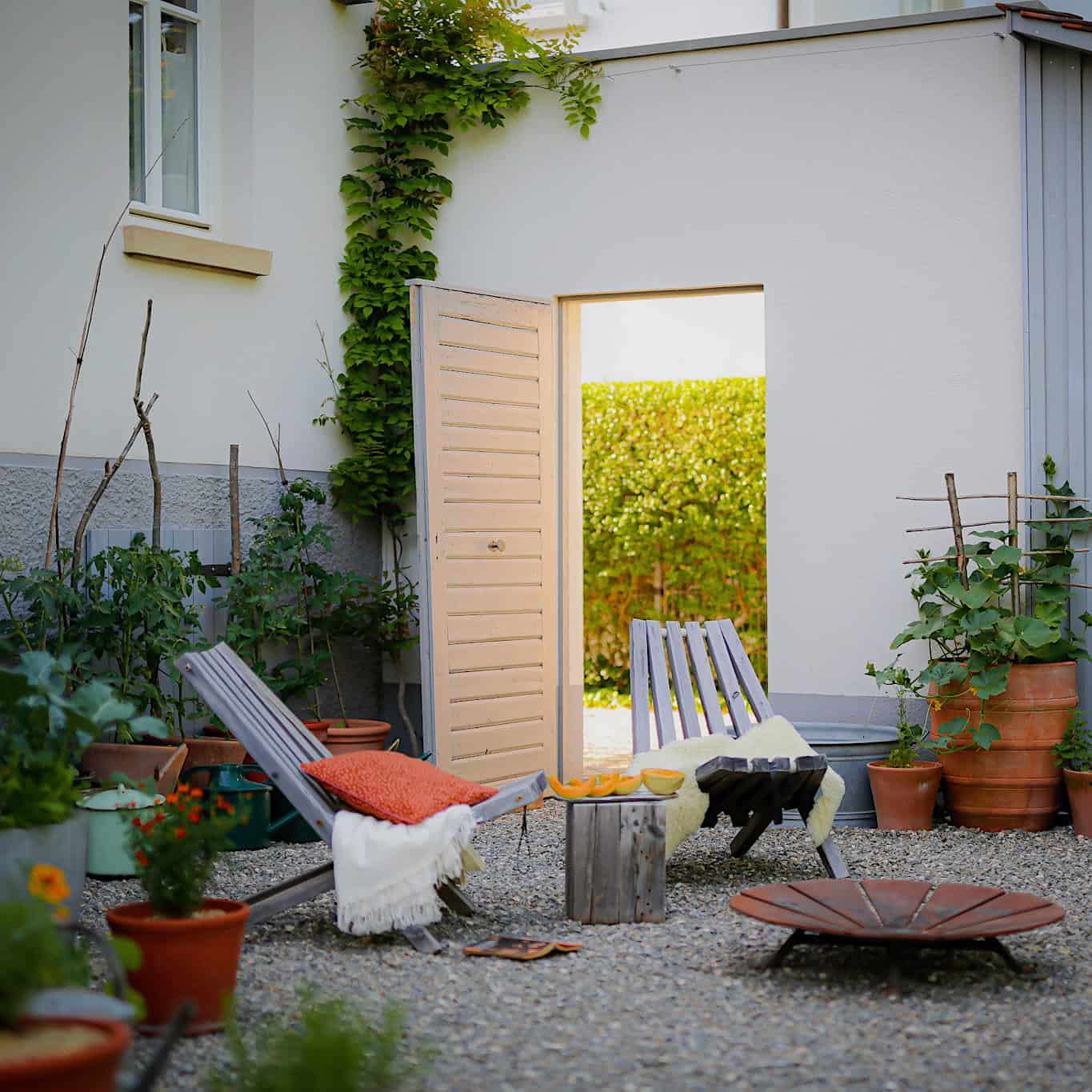 Lounge-Gartenstühle aus Holz neben Feuerschale in Kiesgarten