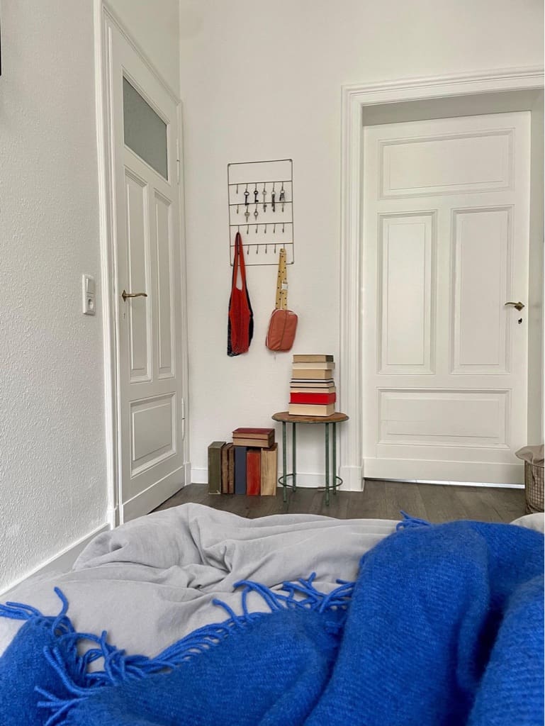 Farbenfrohe Erbstücke und Vintage-Funde (Hocker, Schlüsselhaken) in Schlafzimmer mit blauer Tagesdecke auf Bett