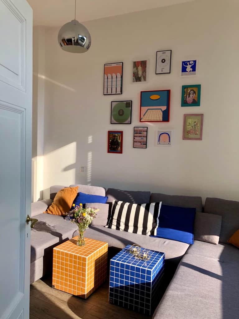 Farbenfrohe Erbstücke und Vintage-Funde in Wohnzimmer mit grauem Eck-Sofa und orange blauen Farbakzenten