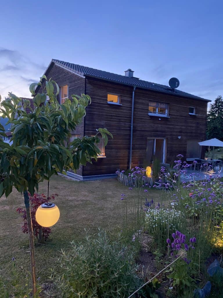 Außenansicht eines Holzhauses mit beleuchtetem Garten in der Dämmerung 