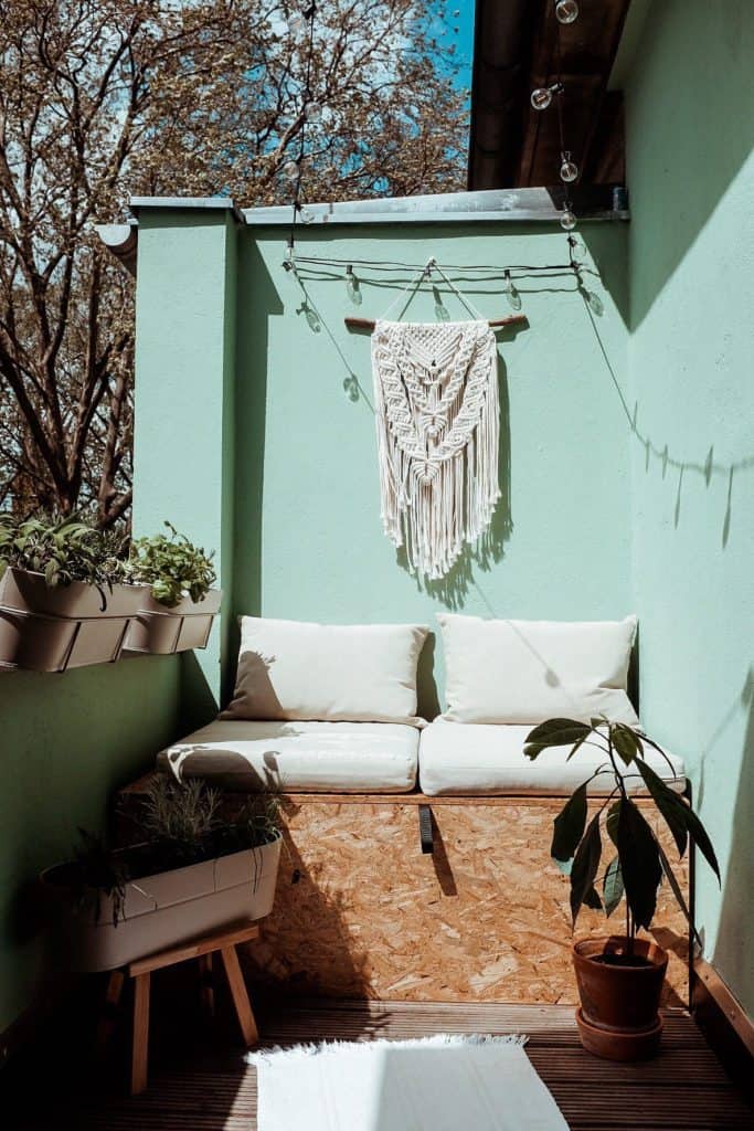 Flohmarktfunde und Designklassiker - Balkon mit Makramee an türkis farbiger Wand über einer kleinen Sitzecke mit weißen Sitzpolstern