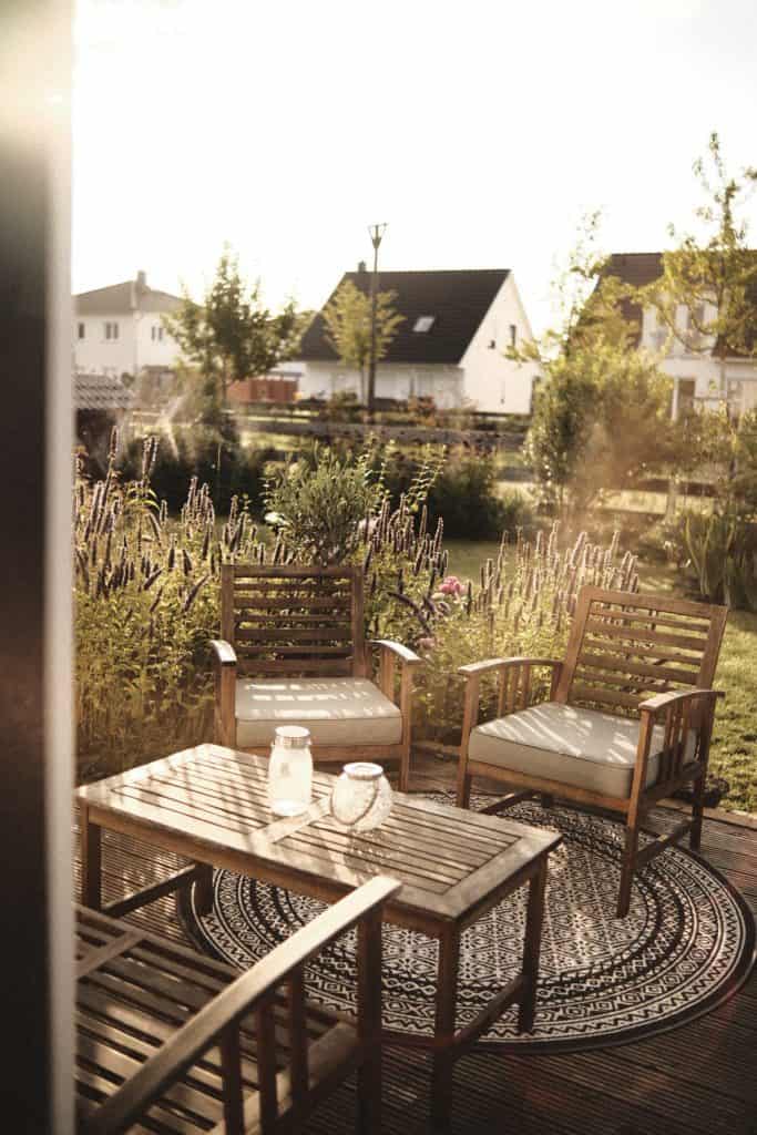 Holzterrasse mit Gartenstühlen und Tisch vor Garten mit Lavendelpflanzen