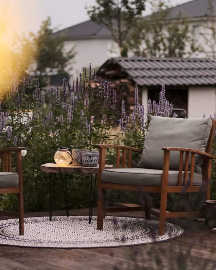 Holzterrasse mit Gartenstühlen und Tisch auf einem runden Teppich mit Muster