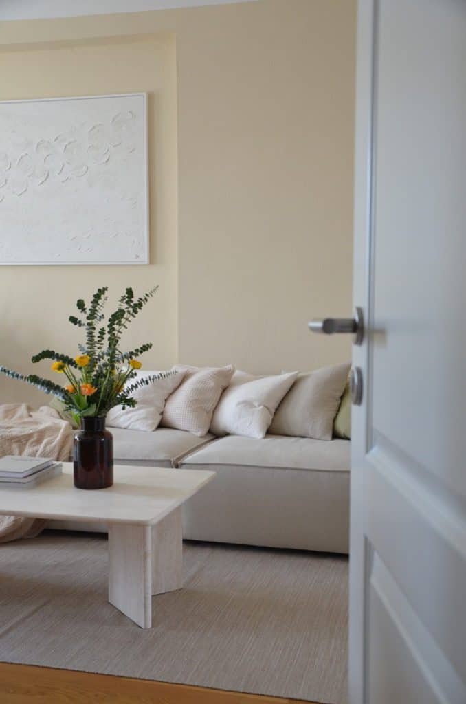 weißgraues Sofa in Wohnzimmer mit hellgelber Wandfarbe und Blumenvase auf Couch-Tisch