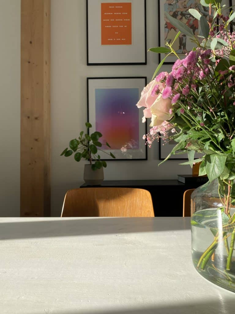 Transparente Vase mit Schnittblumen auf Tisch, im Hintergrund eine Bilderwand mit Prints - Moderne Linien und weiche Formen und Farben