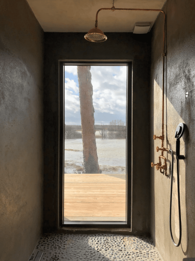 Duschkabine mit raumhohem Fenster mit Blick auf Terrasse und die grüne Natur. 