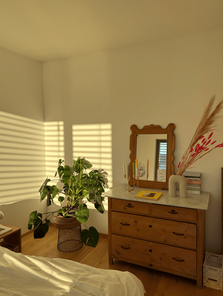 Schlafzimmer mit historischem Holz-Sideboard neben dem große Zimmerpflanze steht