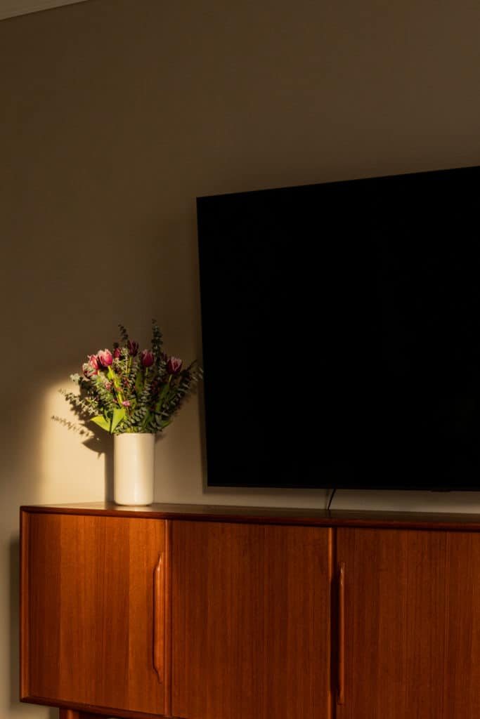 Vintage-Sideboard von Heinrich Riestenpatt auf dem eine weiße Vase mit Schnittblumen steht. Über dem Sideboard hängt ein Fernseher an der Wand- 