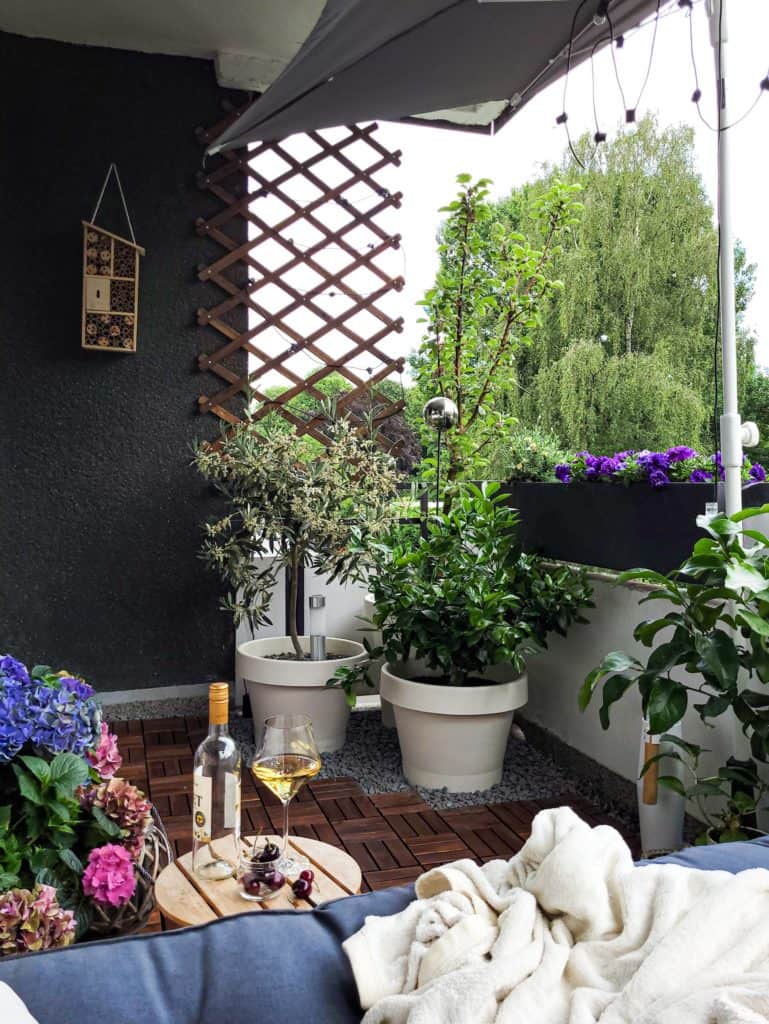 Balkon mit vielen Pflanzen und Holzplatten. Im Vordergrund befindet sich eine Sitzbank mit Polstern,  